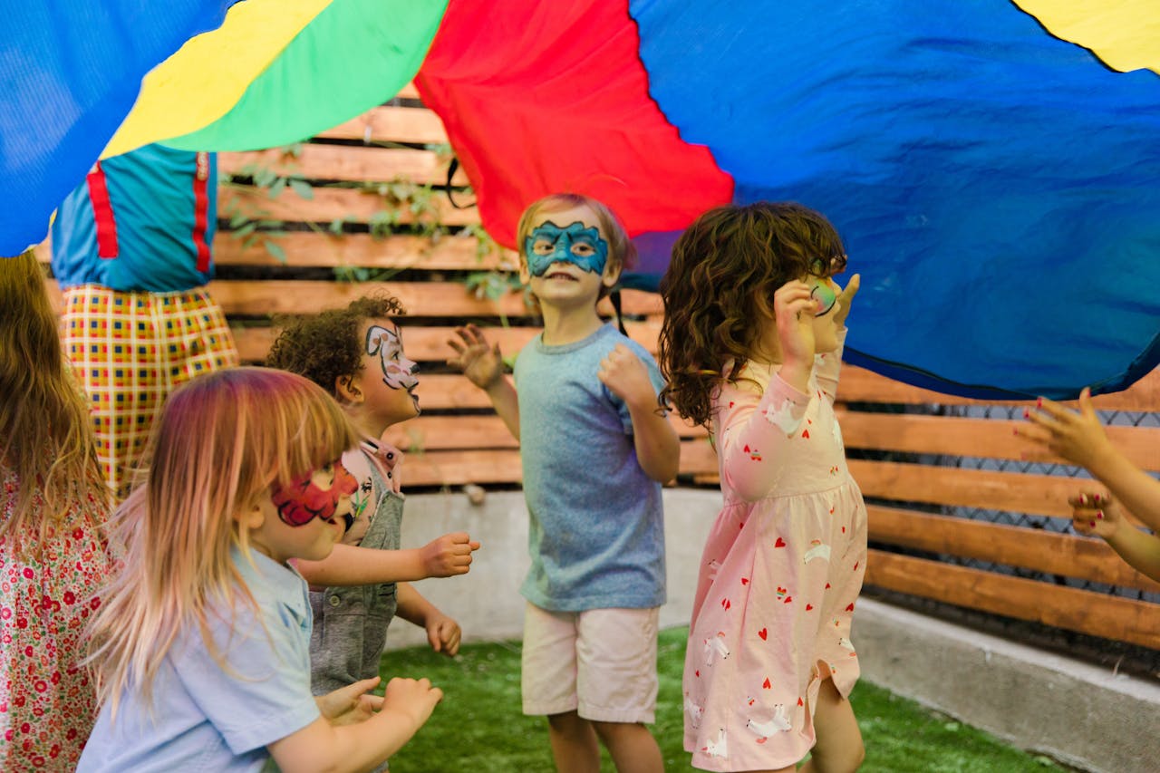 gallery-01 Children with face paint enjoying an outdoor party with vibrant colors and playful activities.
