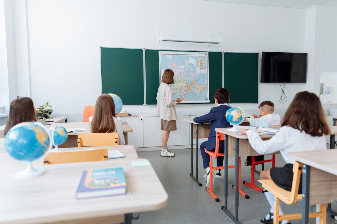 services-02 Students engaged in a geography lesson, focusing on a wall map in a classroom with globes and study materials.