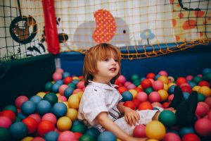 pexels photo 27175469 27175469 A child sits happily in a vibrant ball pit at an indoor play area.